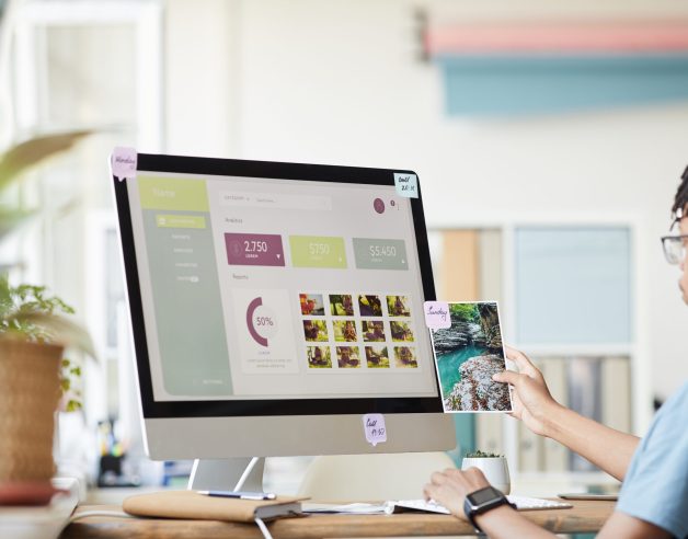 Portrait of young African-American photographer managing photo stock marketplace while using computer at desk in home office with photo website on screen, copy space